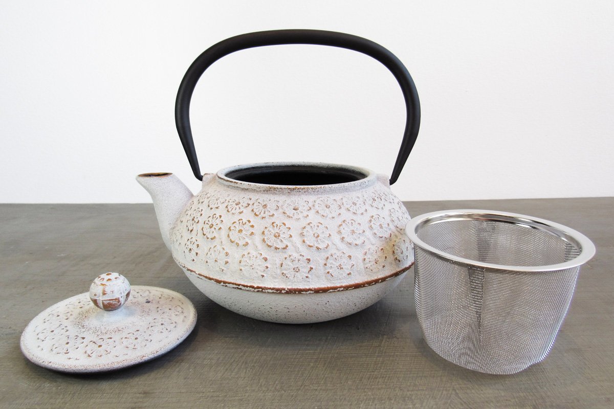 Open white cast iron teapot next to its lid and stainless steel infuser basket