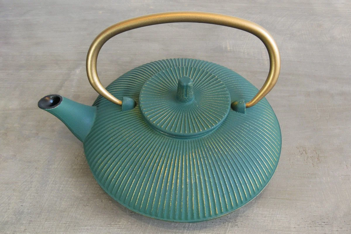 Top-down view of a teal cast iron teapot with a gold handle and gold-brushed vertical stripes