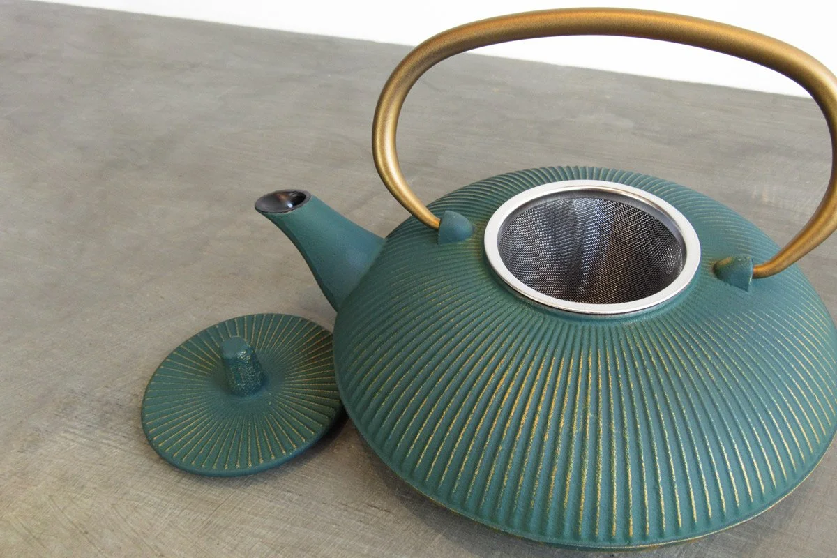 Open teal cast iron teapot showing the stainless steel infuser basket inside