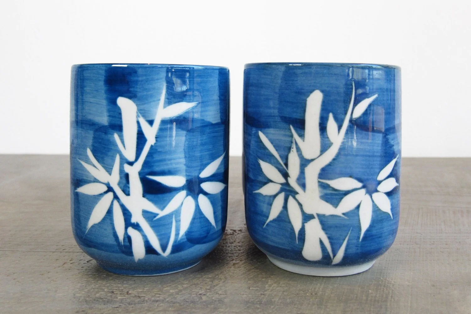 two blue teacups with a white bamboo design placed side by side on a wooden surface