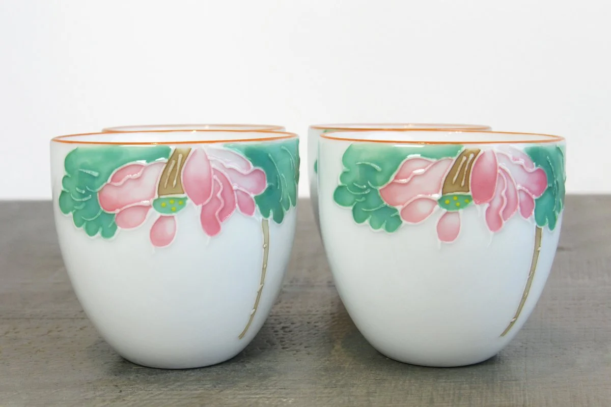 Close-up of four white teacups with a hand-painted pink lotus flower design