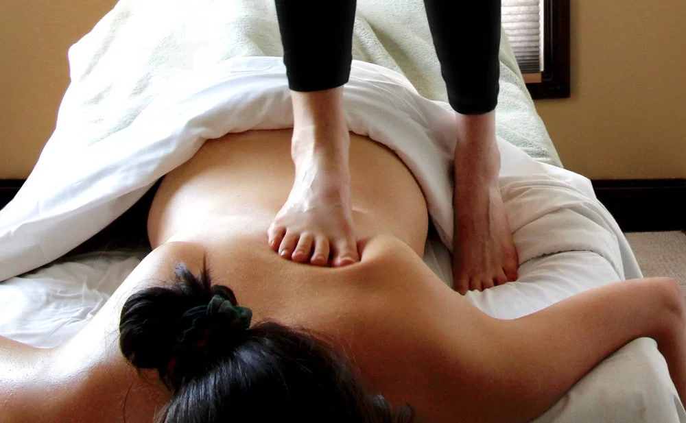 massage therapist using the Ashiatsu back walking technique and applying pressure with their foot on a massage client's back
