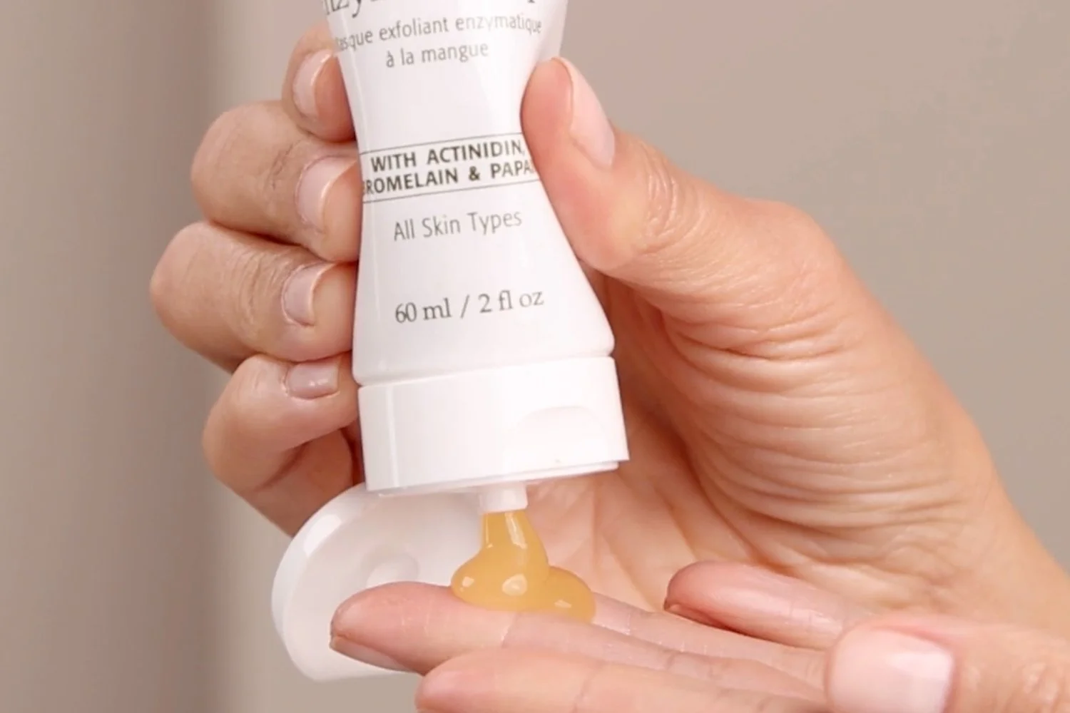 A person squeezing the Eminence Organics Mango Exfoliating Enzyme Masque tube into their hand