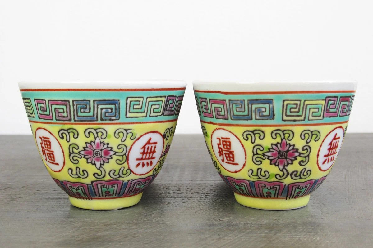 2 light yellow teacups with hand-painted red Chinese characters and multicolor botanical patterns