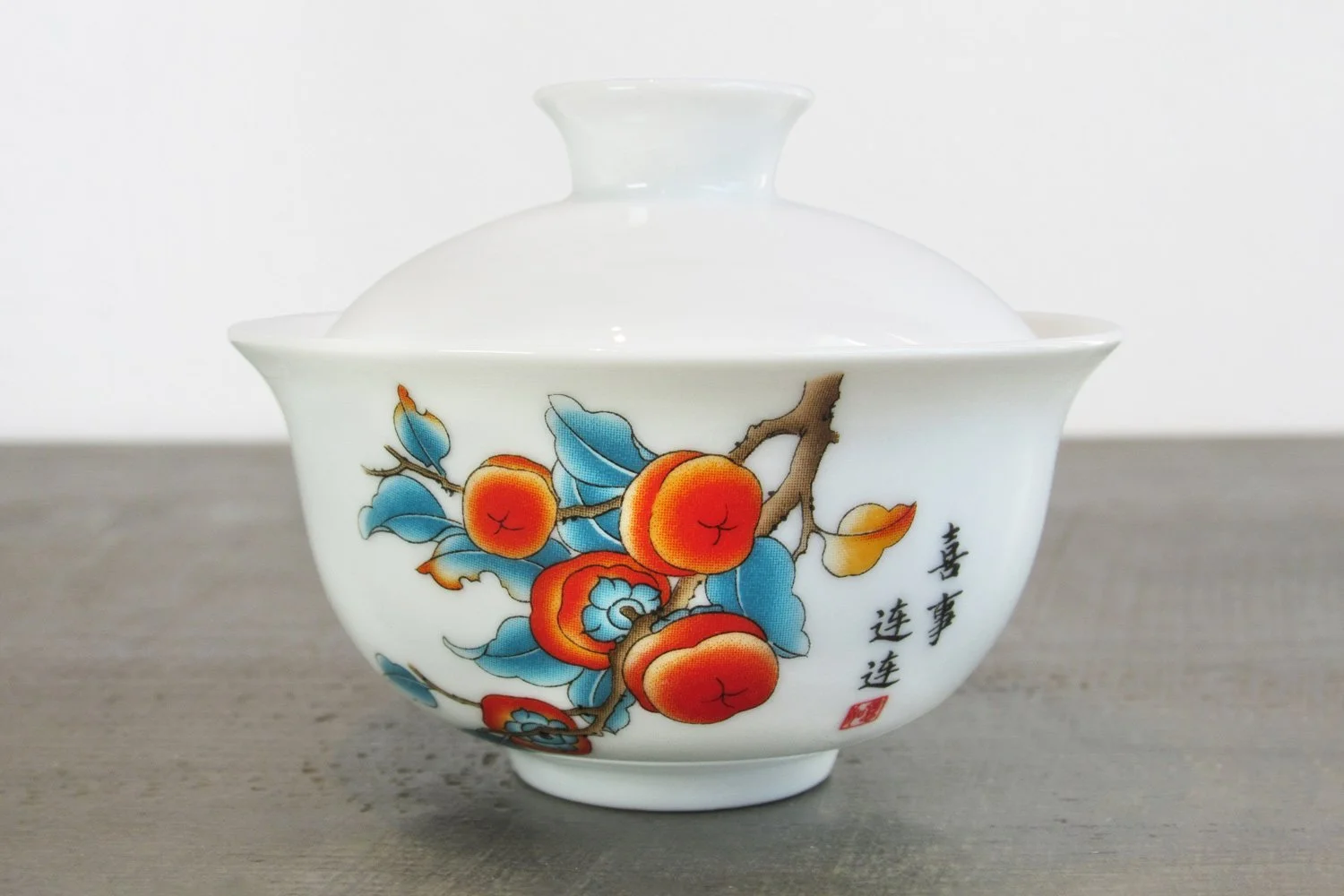 Close-up of a glossy white glaze gaiwan decorated with a vibrant persimmon branch motif
