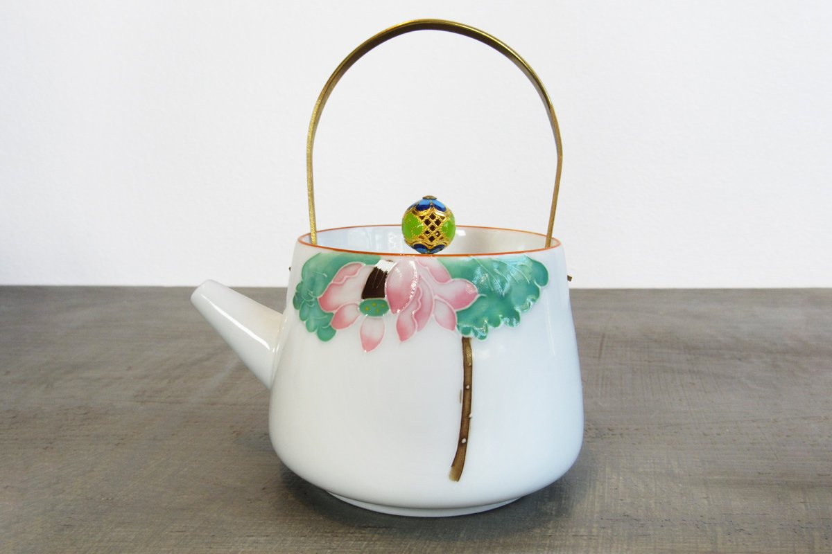 white teapot with a gold handle, ornate gold lid knob, and hand-painted pink lotus flower design