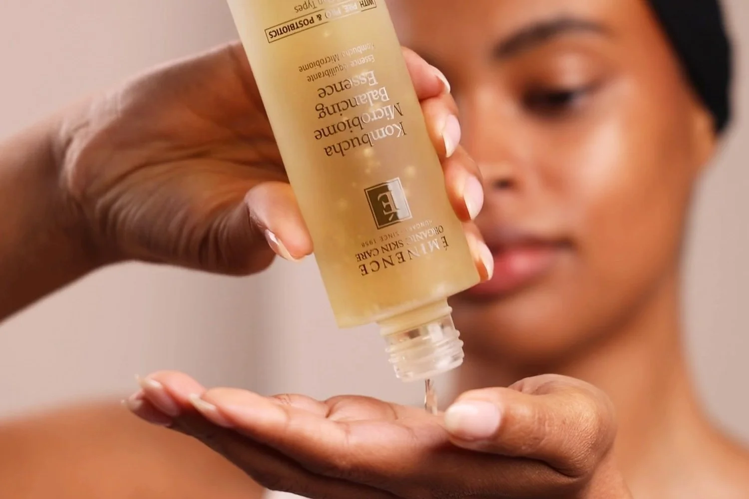 A woman holding the Eminence Organics Kombucha Microbiome Balancing Essence glass bottle and pouring the essence into her hand