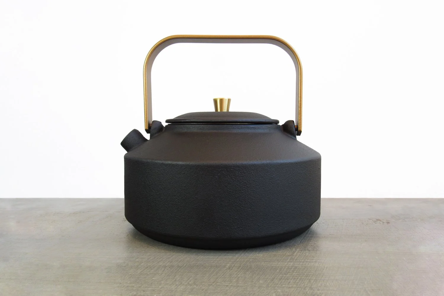 Matte black cast iron teapot with a gold handle and teapot knob