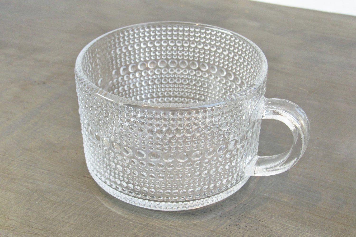 glass teacup with an embossed hobnail texture on a gray wooden surface