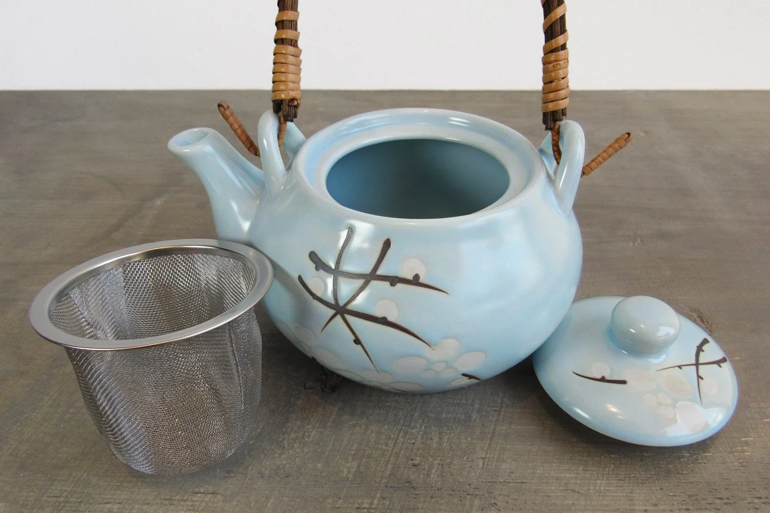 stainless steel tea filter next to a light blue teapot with wrapped rattan handle