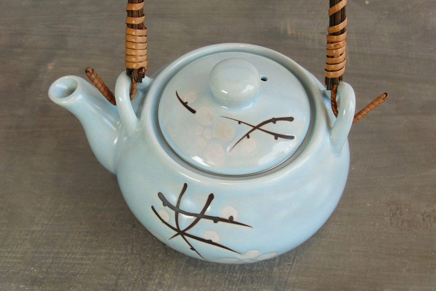top-down view of a light blue glaze teapot with a design of white blossoms and branches