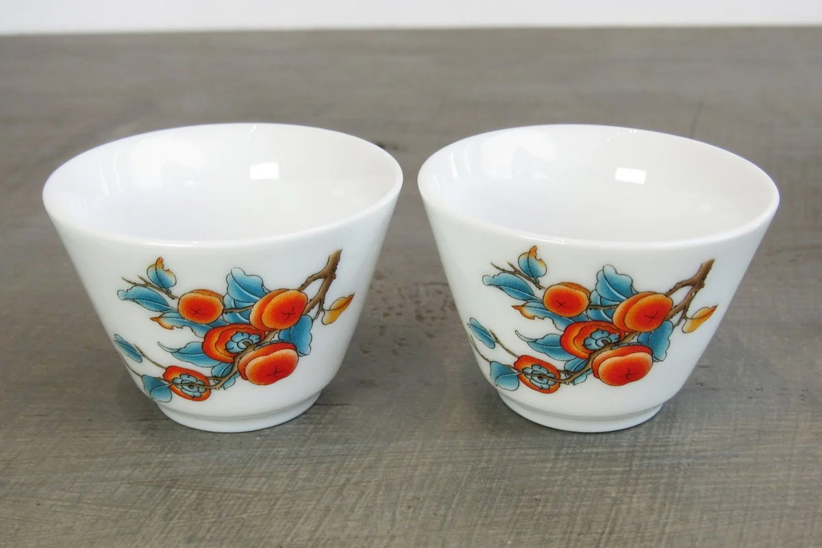 Top-down view of two white teacups decorated with a persimmon pattern