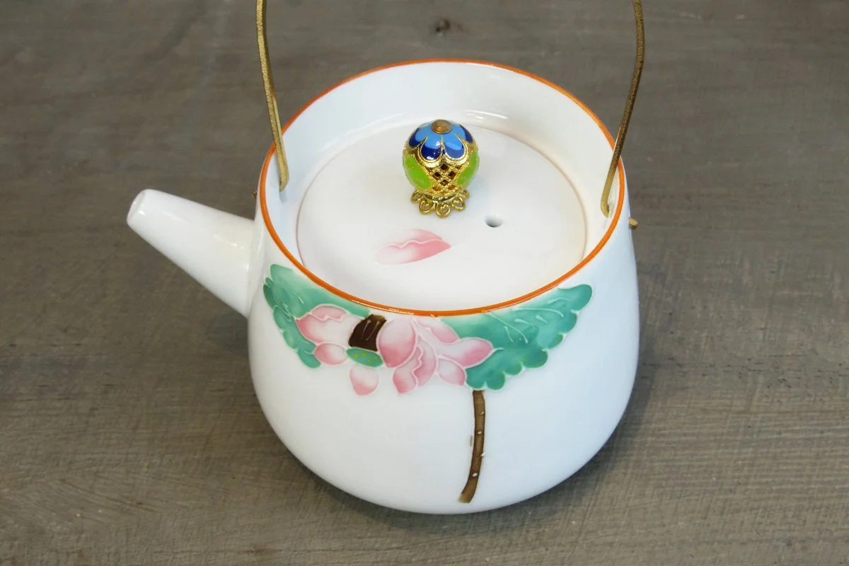Top-down view of a white teapot with a gold handle, ornate gold lid knob, and hand-painted pink lotus flower design