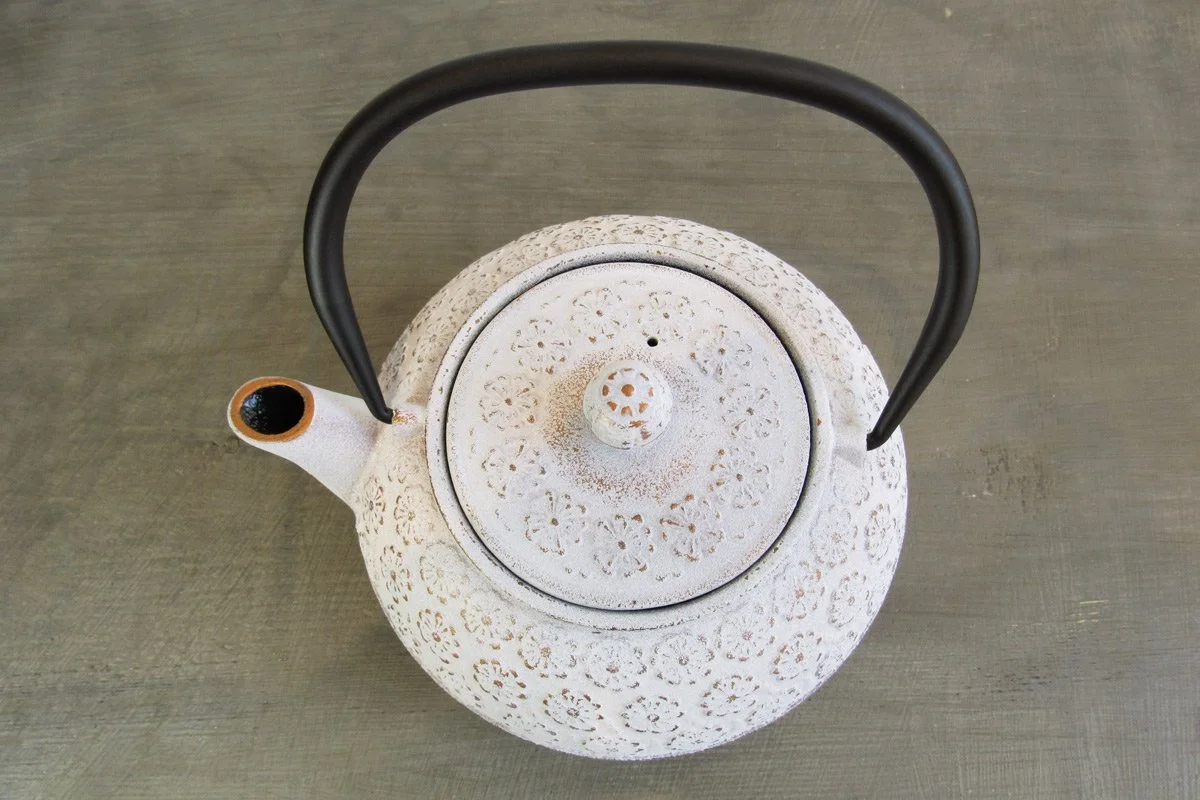 Top-down view of a white cast iron teapot with a textured finish and raised floral details