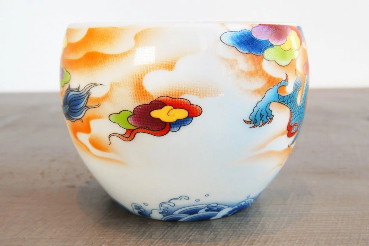Closeup of a teacup with a blue dragon on a background of colorful clouds