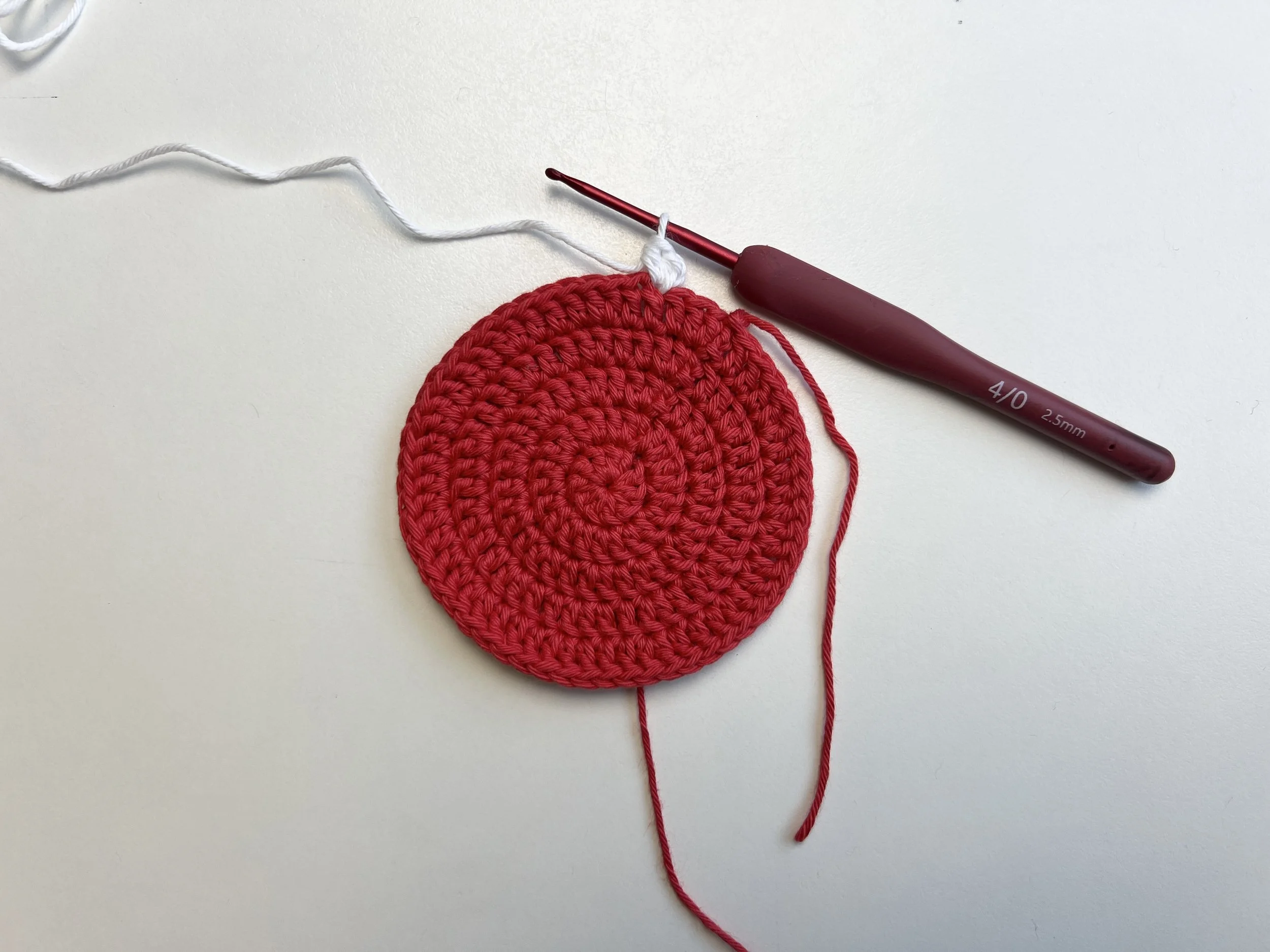  Crocheted flat red circle with white yarn attached for next round. 
