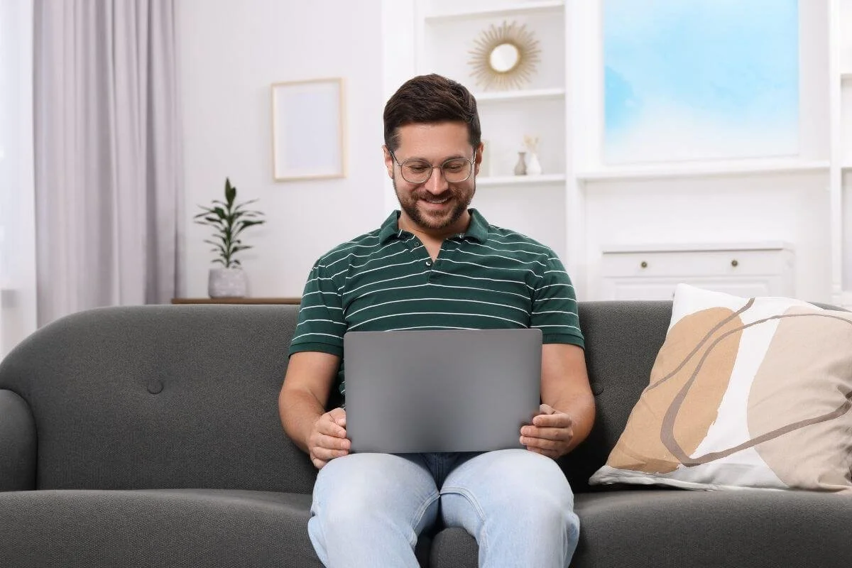 Adult man smiling with a laptop, representing adults seeking neurodiversity affirming ADHD and Autism evaluations at True Reflections MHS in Middlesex NJ