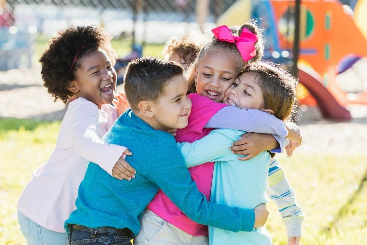 Four diverse children hugging and playing together on a playground representing the age groups served for neurodiversity affirming ADHD and Autism evaluations at True Reflections MHS in Middlesex NJ