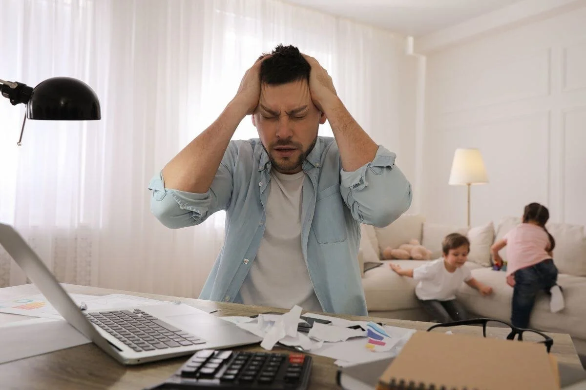 Adult man struggling to focus on work while children play in the background illustrating how undiagnosed ADHD affects concentration and daily functioning for adults in New Jersey