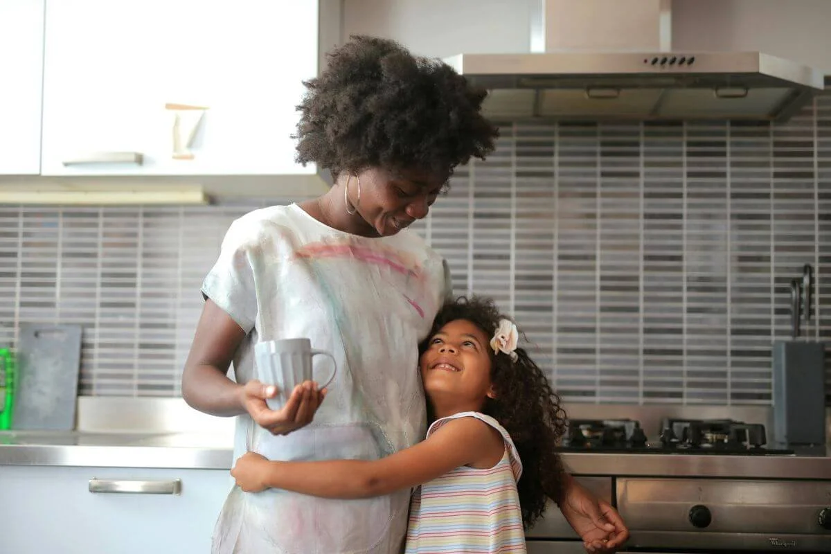 Black mother and daughter hugging and smiling together in the kitchen representing families seeking neurodiversity affirming ADHD and Autism evaluations for girls at True Reflections Mental Health Services in Middlesex NJ