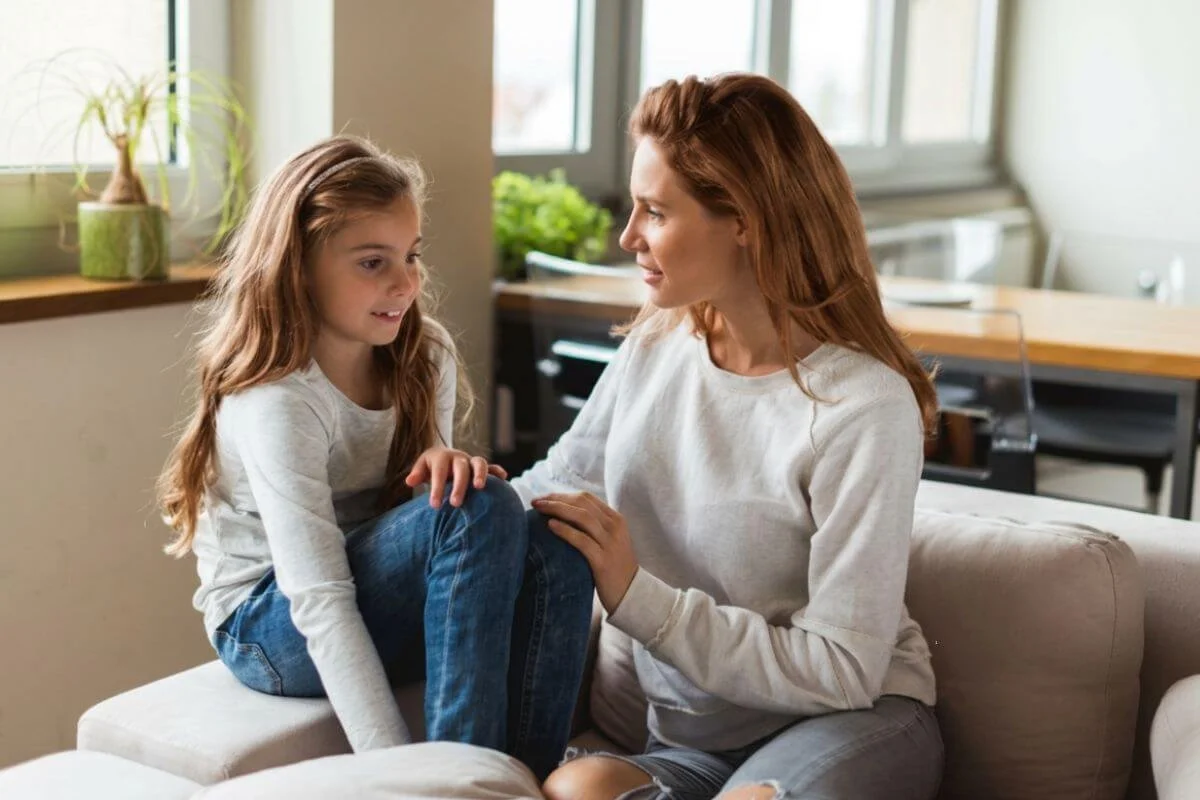 A mother sitting on the couch listening closely to her daughter, representing the importance of understanding a child's neurodevelopmental needs