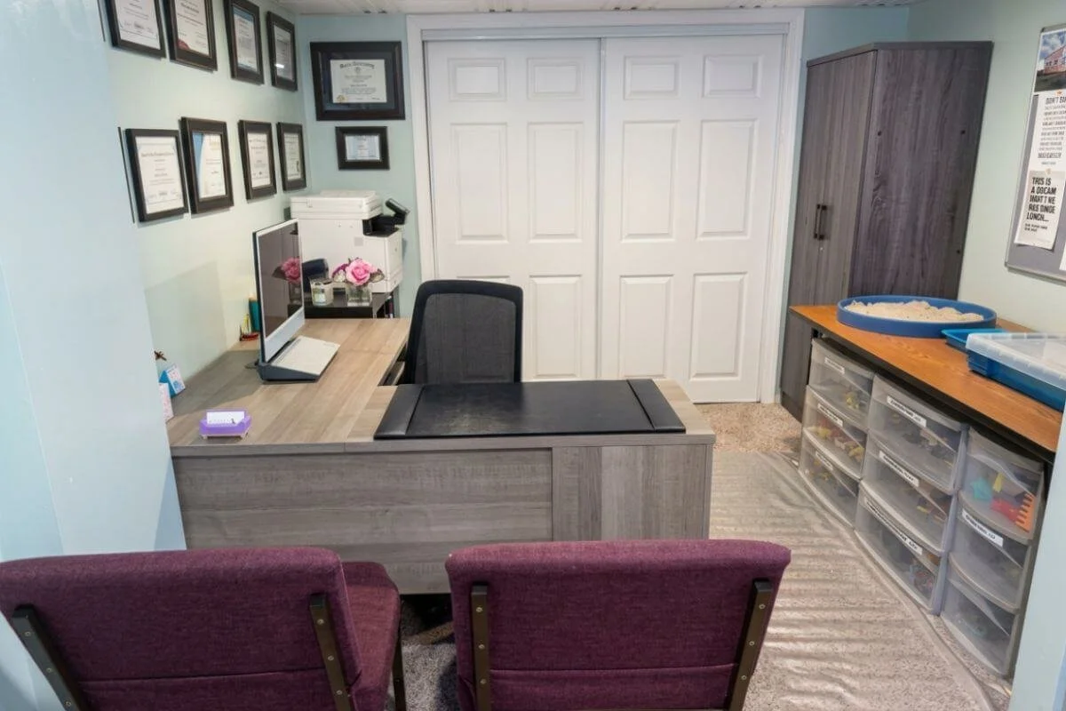 Therapy office at True Reflections Mental Health Services in Middlesex, NJ, showing credential wall, sandtray therapy materials, and client seating