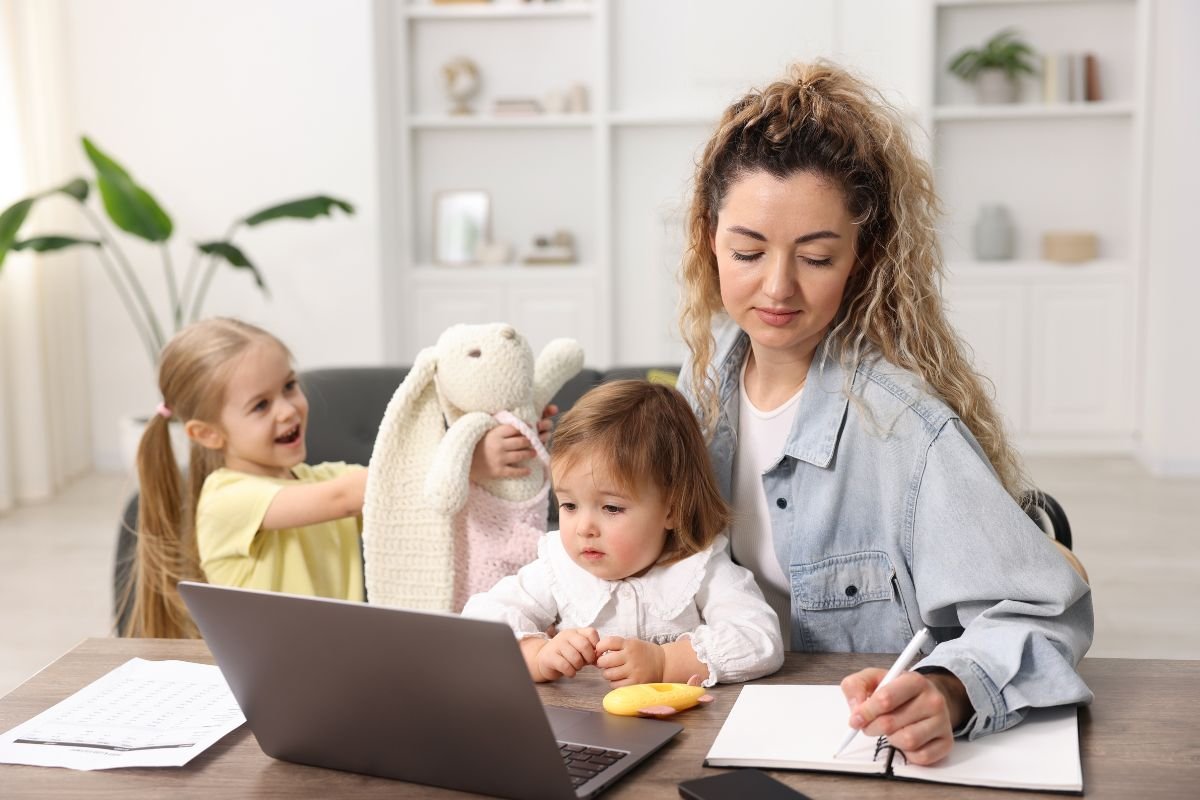 woman sitting at desk writing on notepad with two girls. If you are a woman with ADHD and are struggling with executive functioning, ACT Therapy in Middlesex NJ can help you.