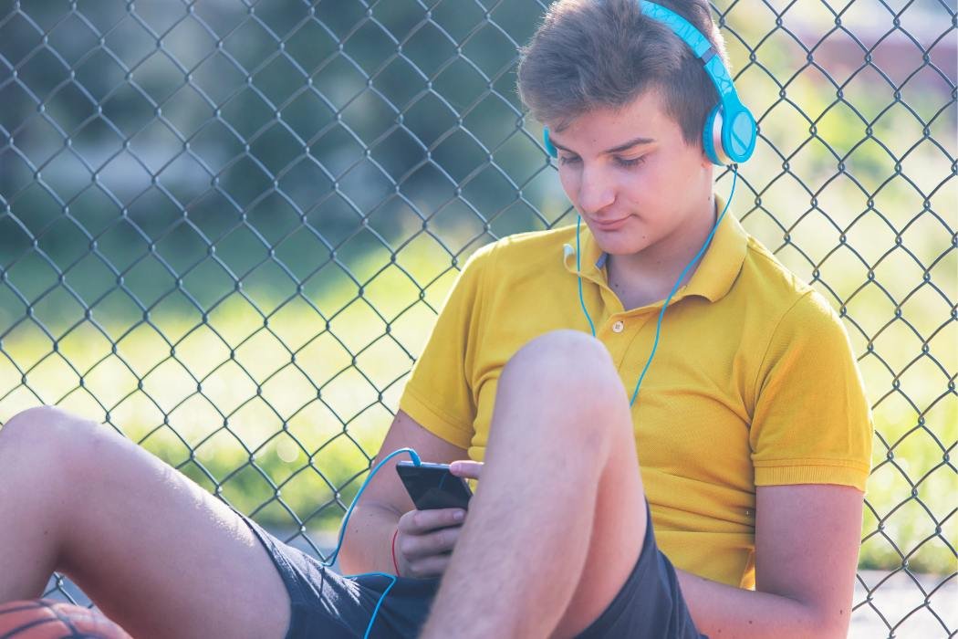 Child sitting against a fence listening to headphones representing children served by neurodiversity affirming ADHD and Autism evaluations and therapy at True Reflections Mental Health Services in Middlesex NJ