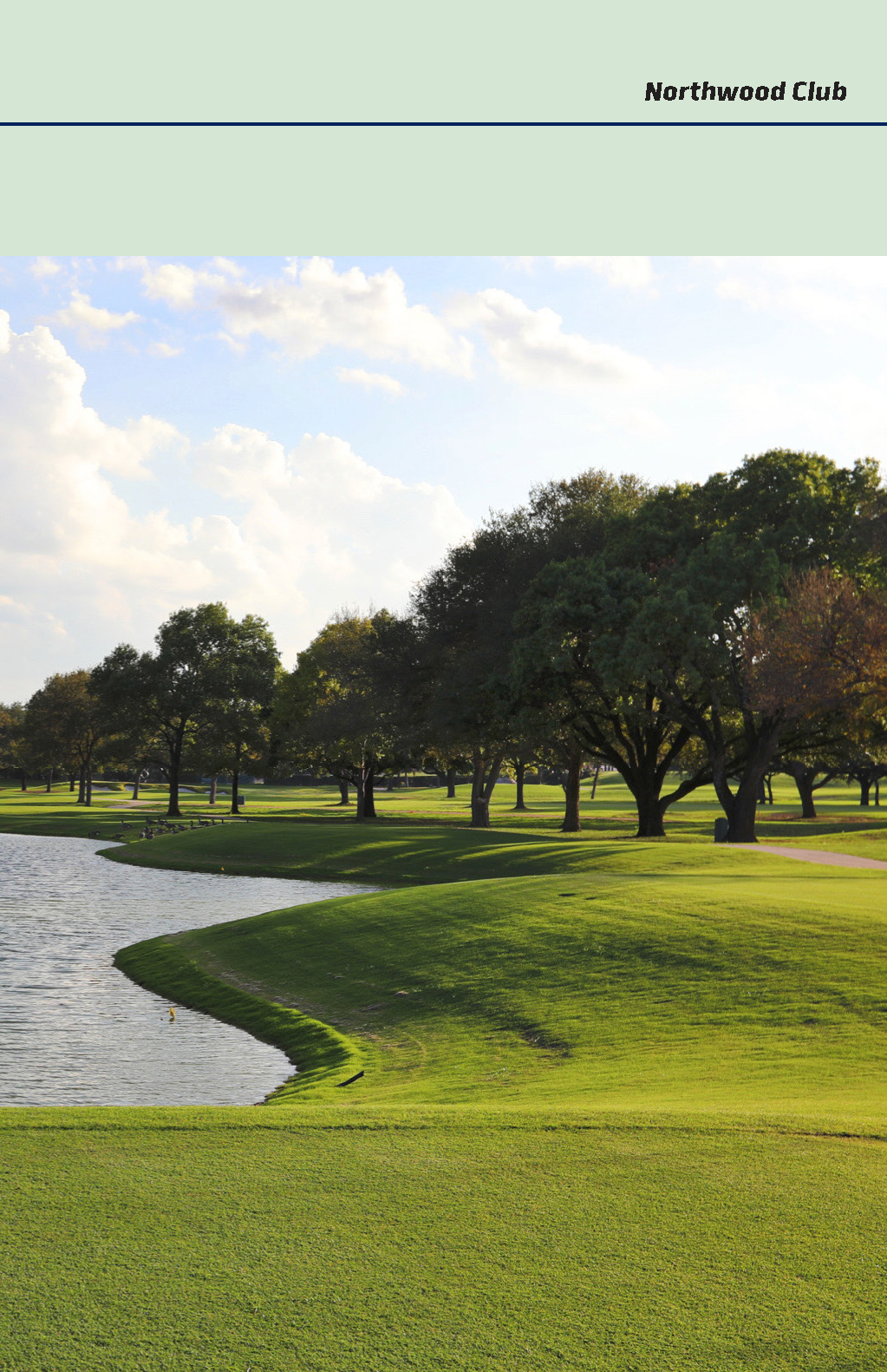 A scenic view of a well-maintained golf course with lush green grass, tall trees, and a small body of water under a partly cloudy sky.