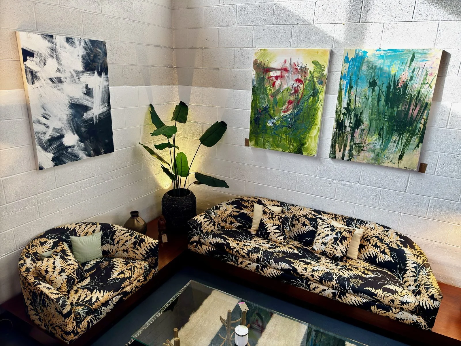 Four abstract paintings hung on a white block wall above two couches.