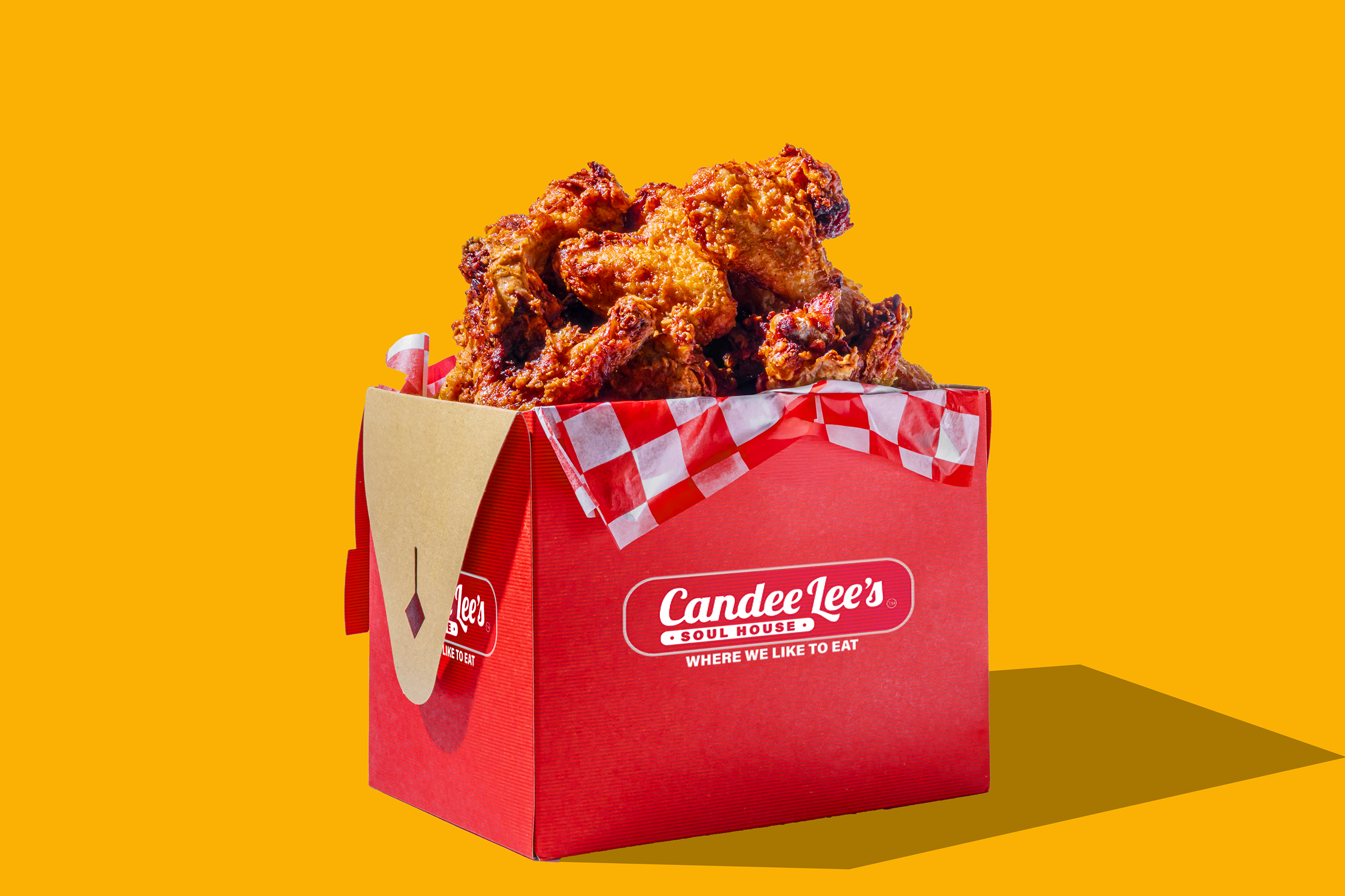 A red box of fried chicken from Candee Lee's Soul House with chicken pieces inside on a yellow background.