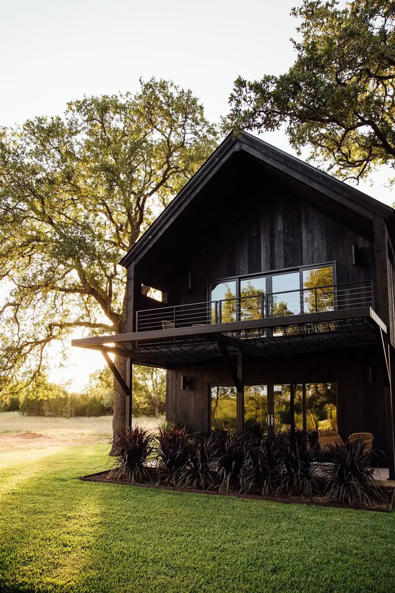 Black two-story hammock lodge at NowHere in the Texas Hill Country, with a suspended net deck, glass doors, and oak trees.