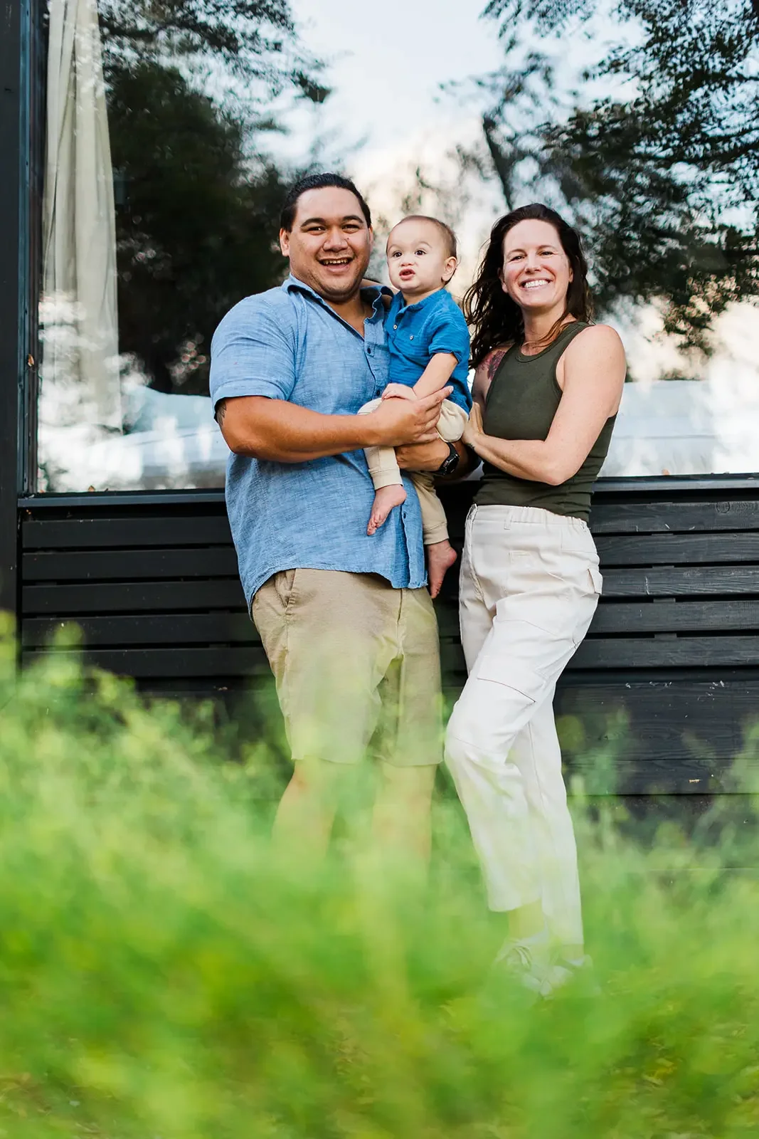 Erika's family smiling together, a man holding a baby beside a woman, in front of a cabin's large glass window