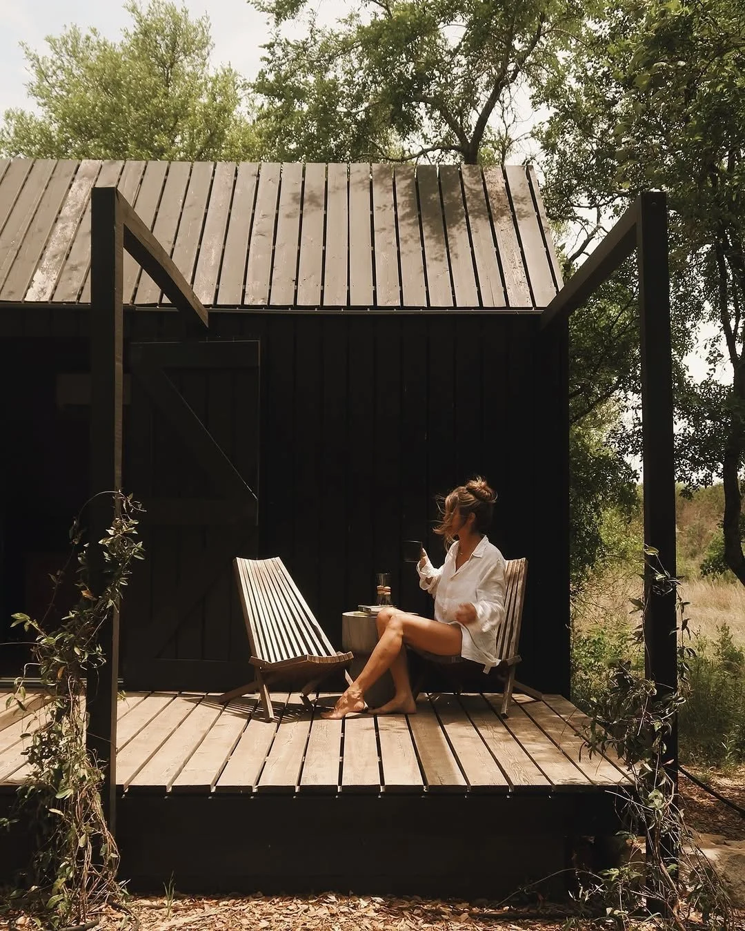 A guest sits in a wooden chair with a mug on the deck at NowHere.