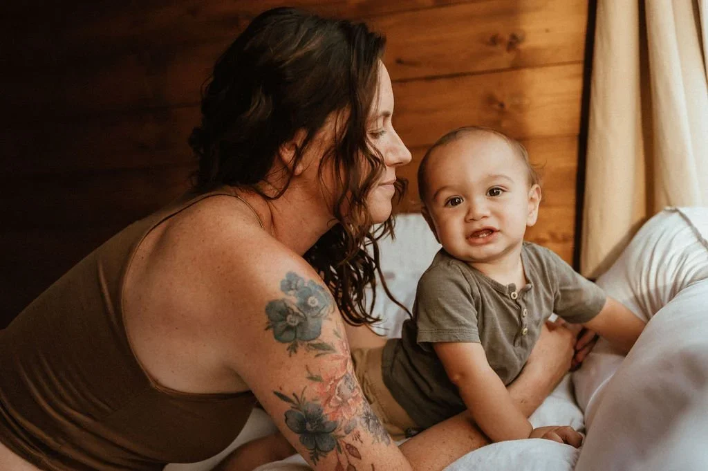 Erika holding her baby on a bed with white bedding, in front of a wood-paneled wall