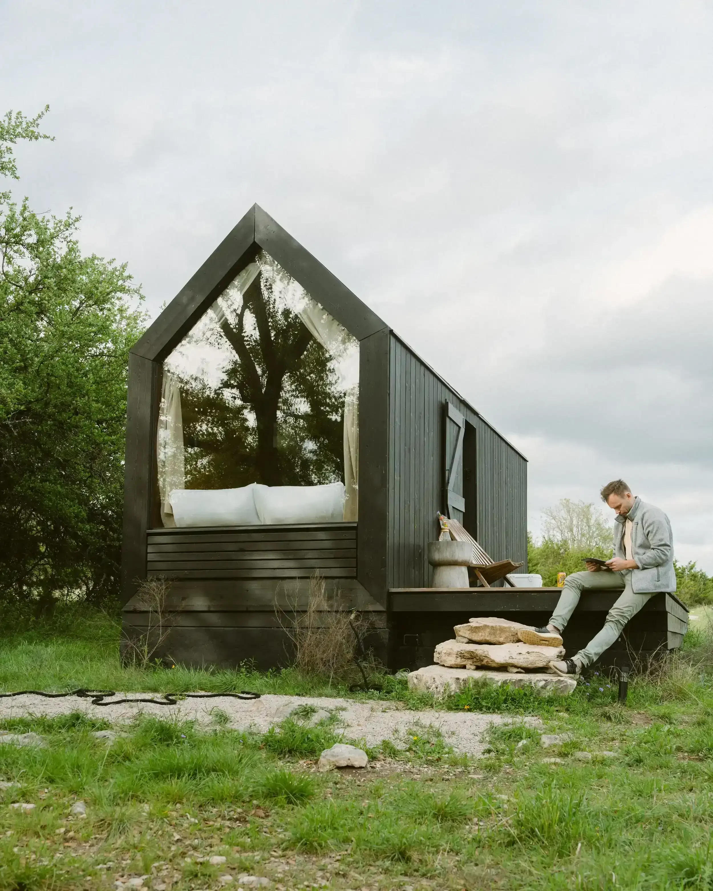 A man sits outside a black A-frame cabin at NowHere in the Texas Hill Country.