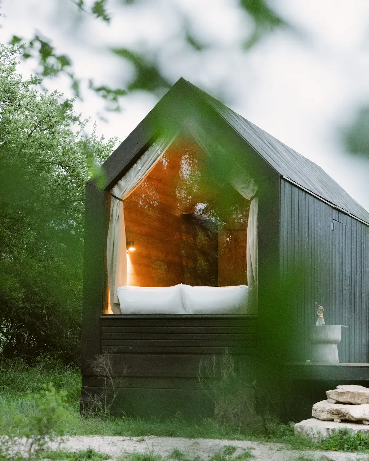 The Mesquite cabin features a large triangular window with white curtains, a bed, and warm wood-paneled walls.