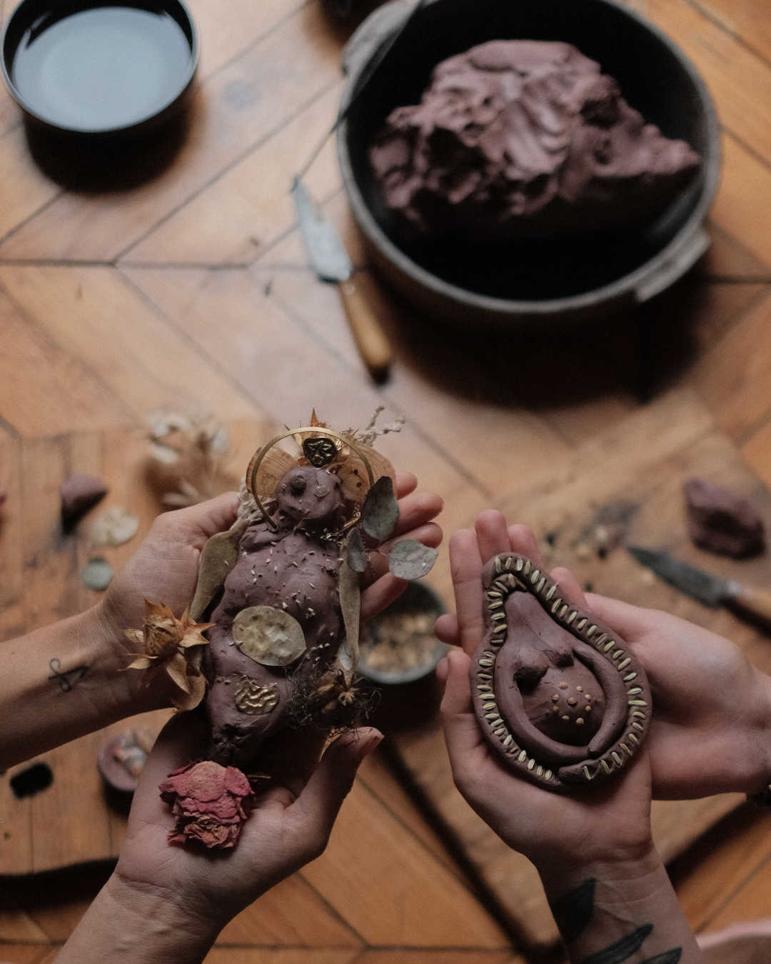 Two people holding a carved sweet potato and a decorated gourd. The sweet potato has various adornments, including leaves, a small statue, and other decorations. The gourd is decorated around the rim with small carved patterns.