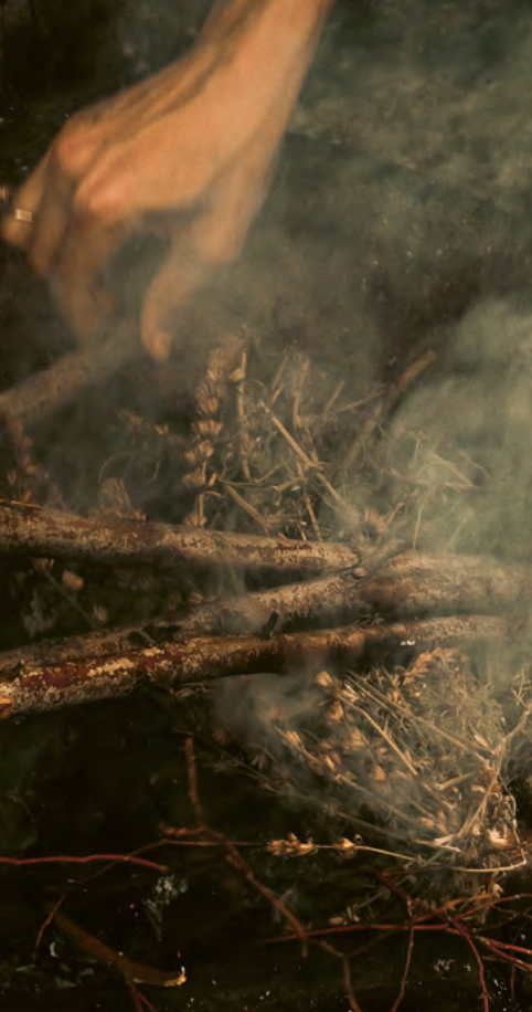 Close-up of a small fire with burning wood and smoke, with some rocks and twigs around the flames.