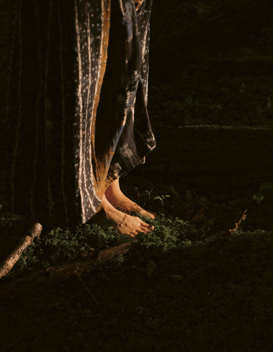 Person crouching outdoors behind a large tree at night, with hands on the ground and partially obscured by the tree.