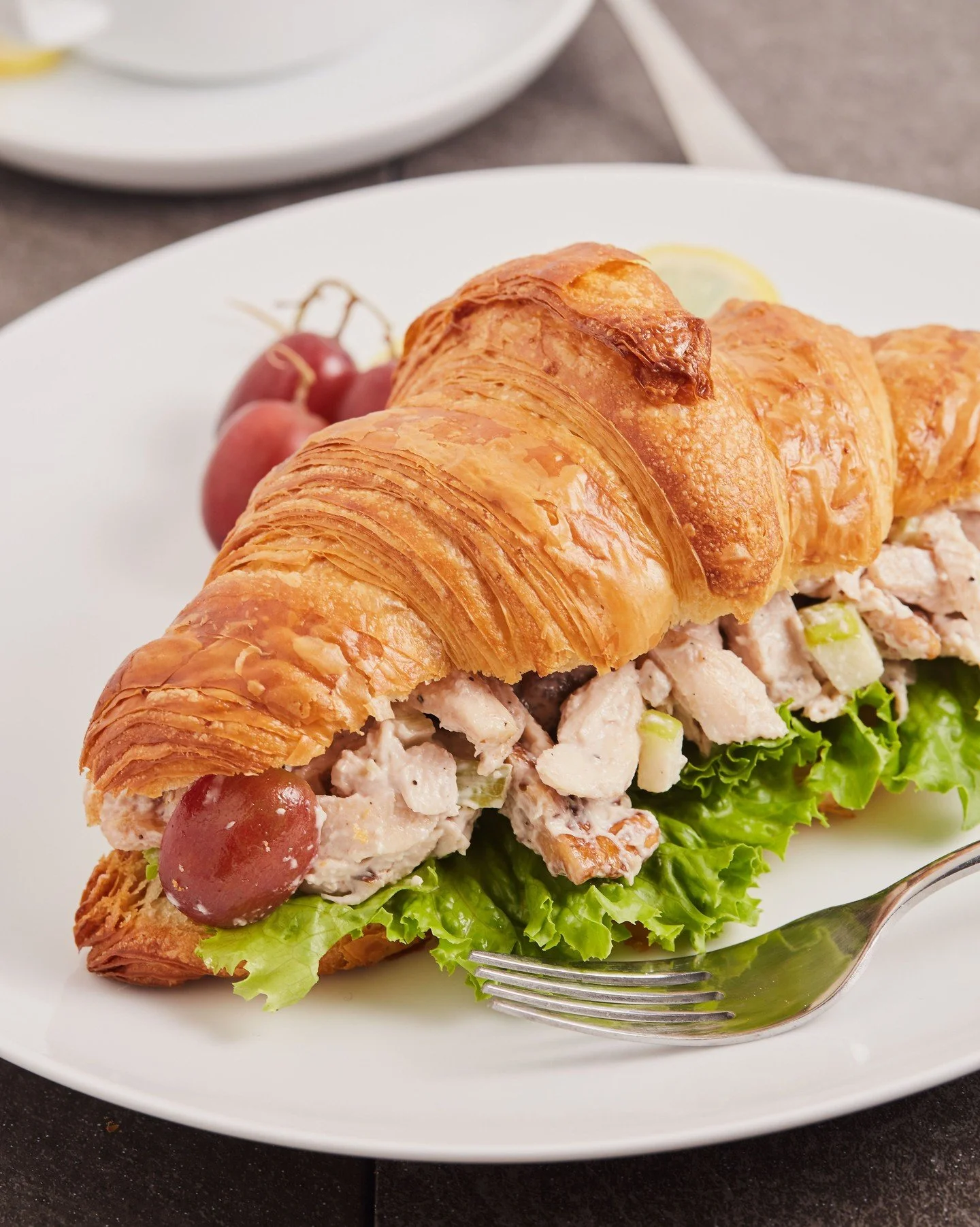 To make our Waldorf Chicken Salad, we oven-roast chicken breast and combine it with freshly sliced celery, green apple, grapes, and walnuts, folding it into a creamy and flavorful mix. We serve it on our signature croissant with green leaf lettuce fo