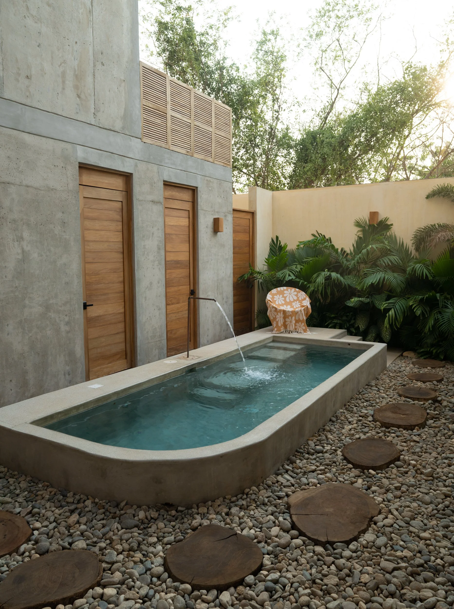 A modern outdoor shower with a built-in pool surrounded by stones and lush greenery.