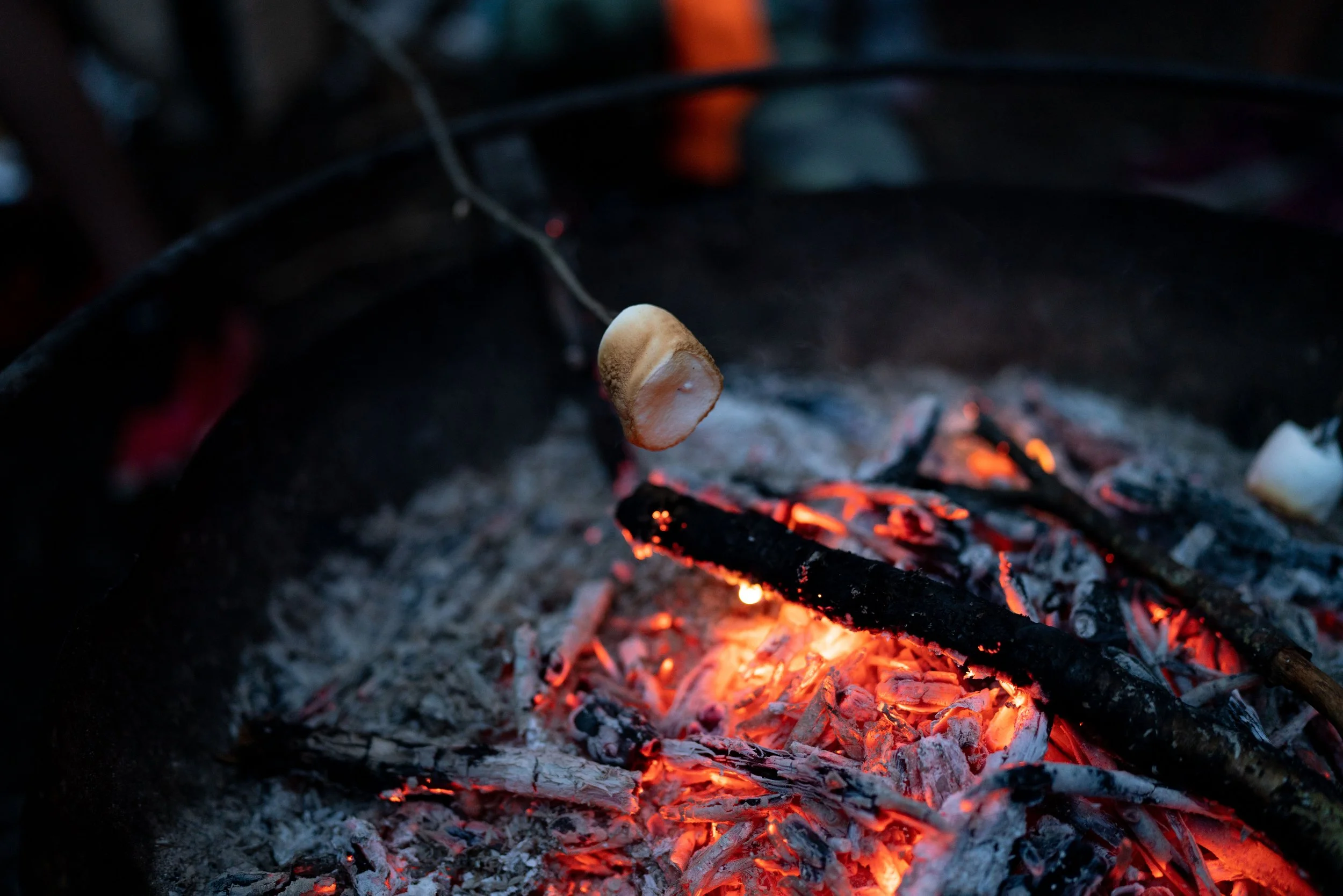 Close-up of a marshmallow being roasted over glowing red hot coals in a fire pit.