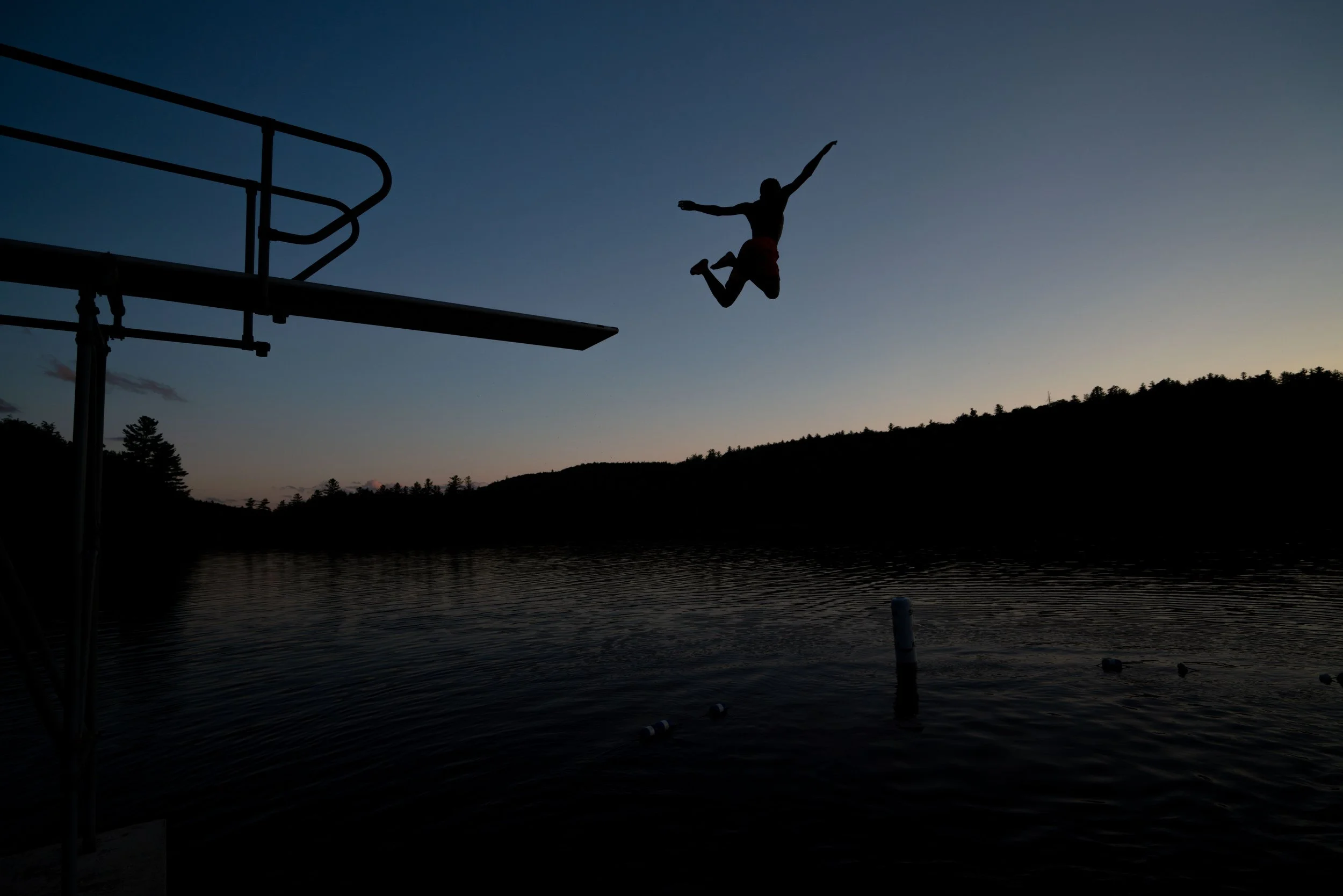 A person jumping into a body of water at sunset, silhouetted against the evening sky.