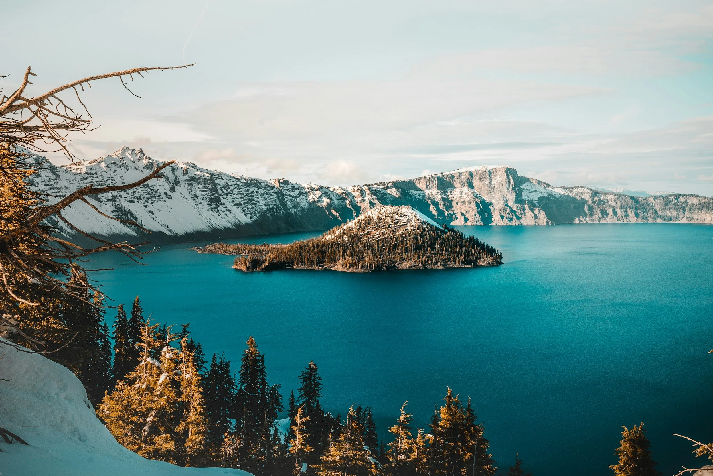 A lake with clear blue water, surrounded by snow-capped mountains and a forest of evergreen trees in the foreground.