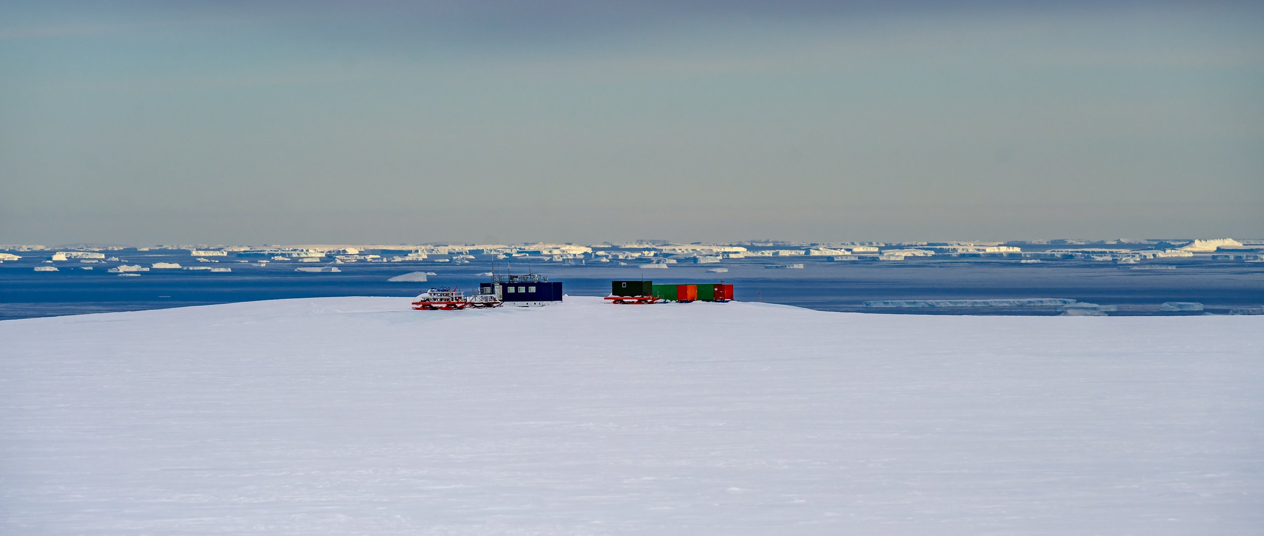 C659 - 12th of November 2022 11:06 am - view from Casey Skiway across to the winterised Skiway buildings to the distant icebergs in Newcomb Bay 