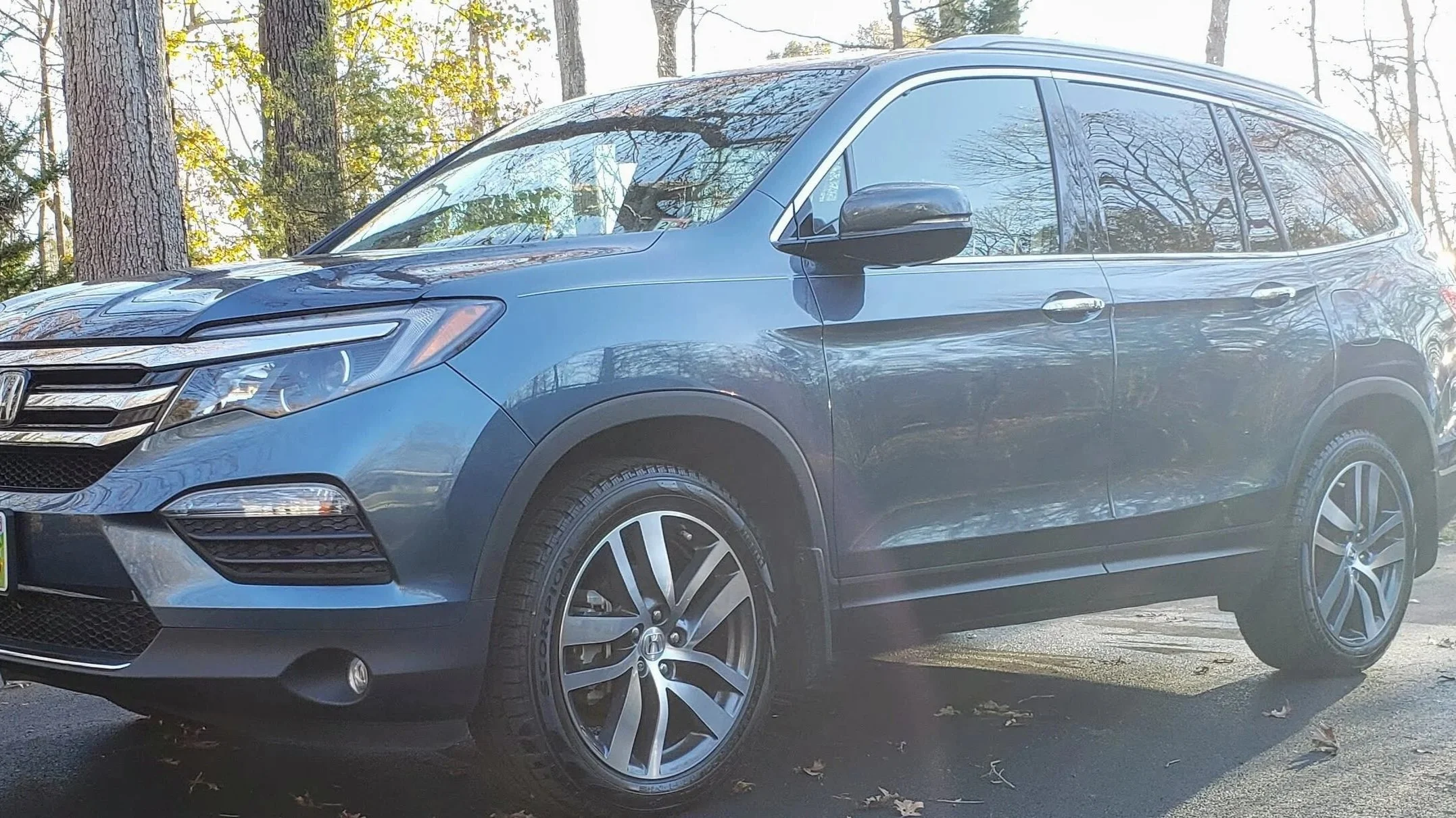 A dark gray Honda SUV parked outdoors among trees with sunlight reflecting on the windows.