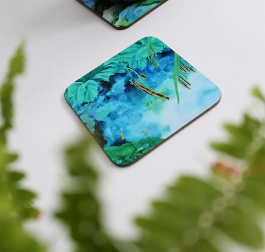A vibrant and glossy bright blue and green coaster featuring a print of an original painting inspired by the plants and water reflections at the Bolfracks pond in Aberfeldy