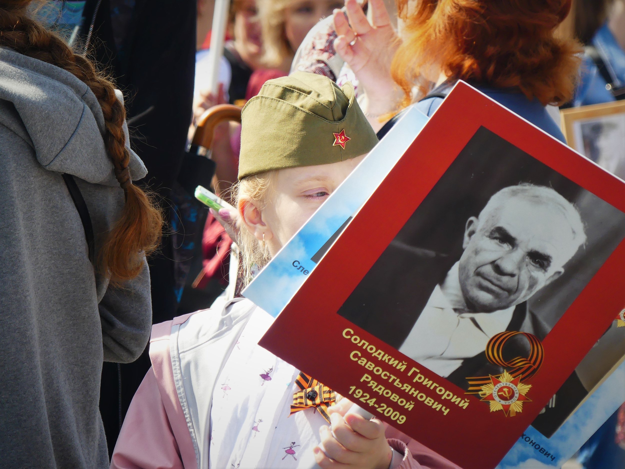  A little girl holds a portrait of a man, likely her ancestor, who fought in the Great Patriotic War (World War II). 