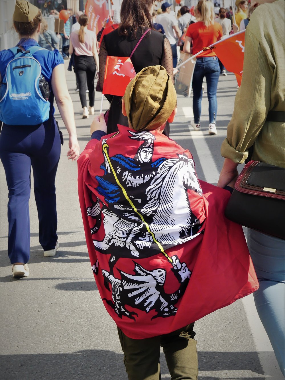  A little boy wrapped in a flag with Moscow’s coat of arms, featuring Saint George, waves a small Soviet flag. 